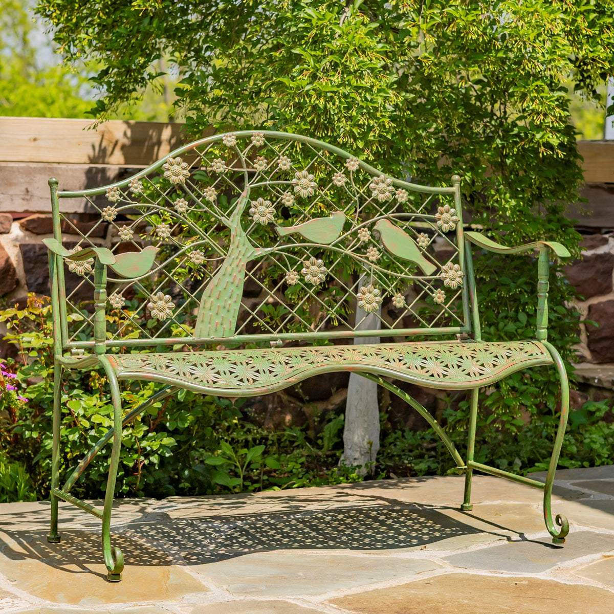 Green metal bench with a flowering tree and bird motifs across its lattice back and perforated seat.