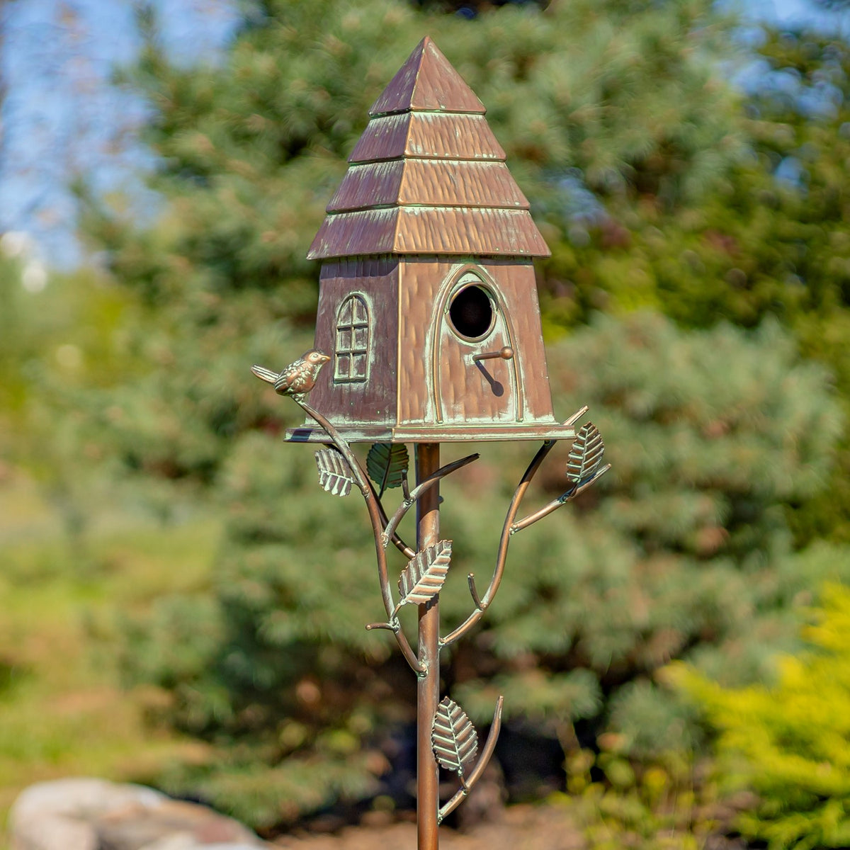 Antique copper birdhouse and decorative iron stake shown close up in a garden