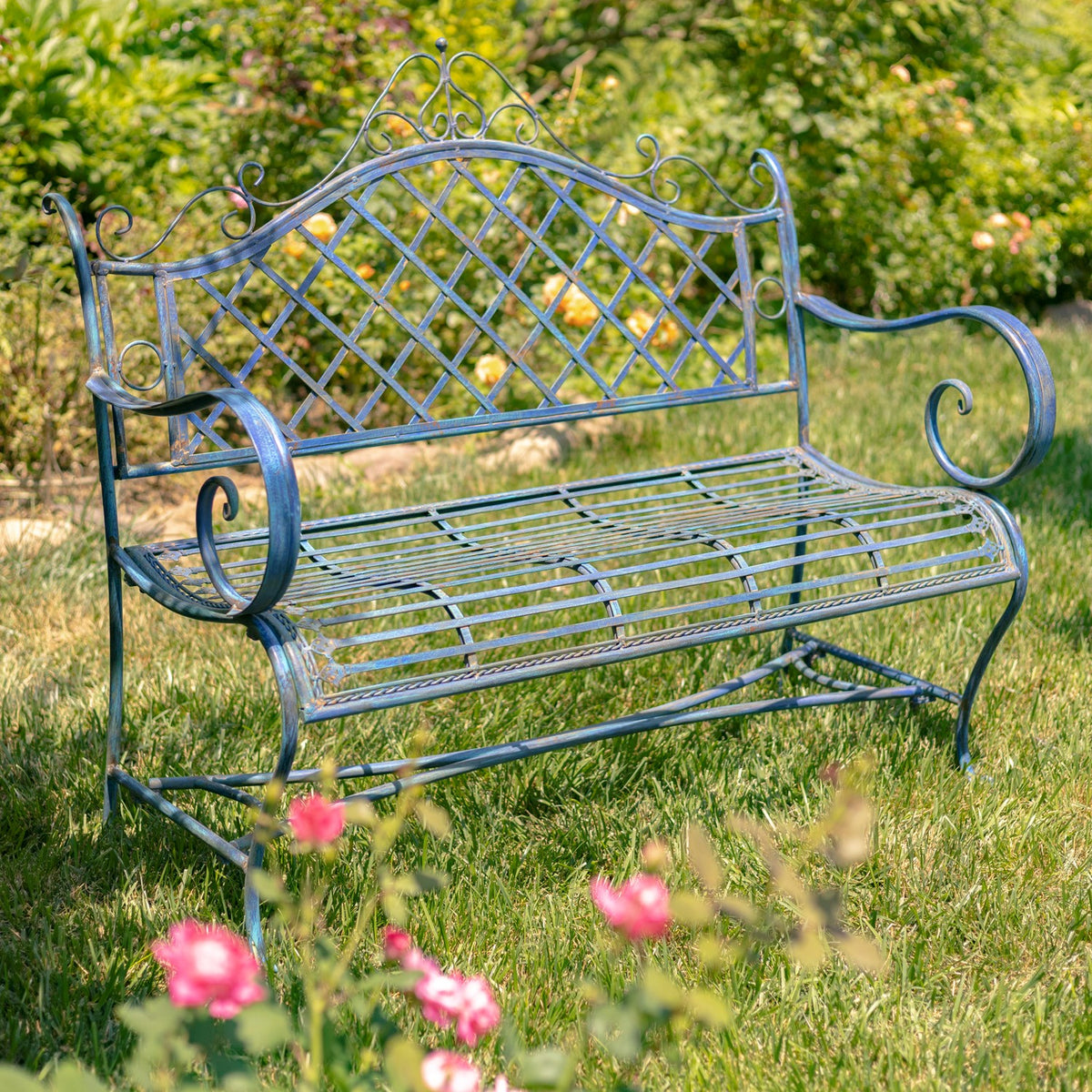Cobalt blue iron garden bench angled in a grassy garden with flowers in the foreground