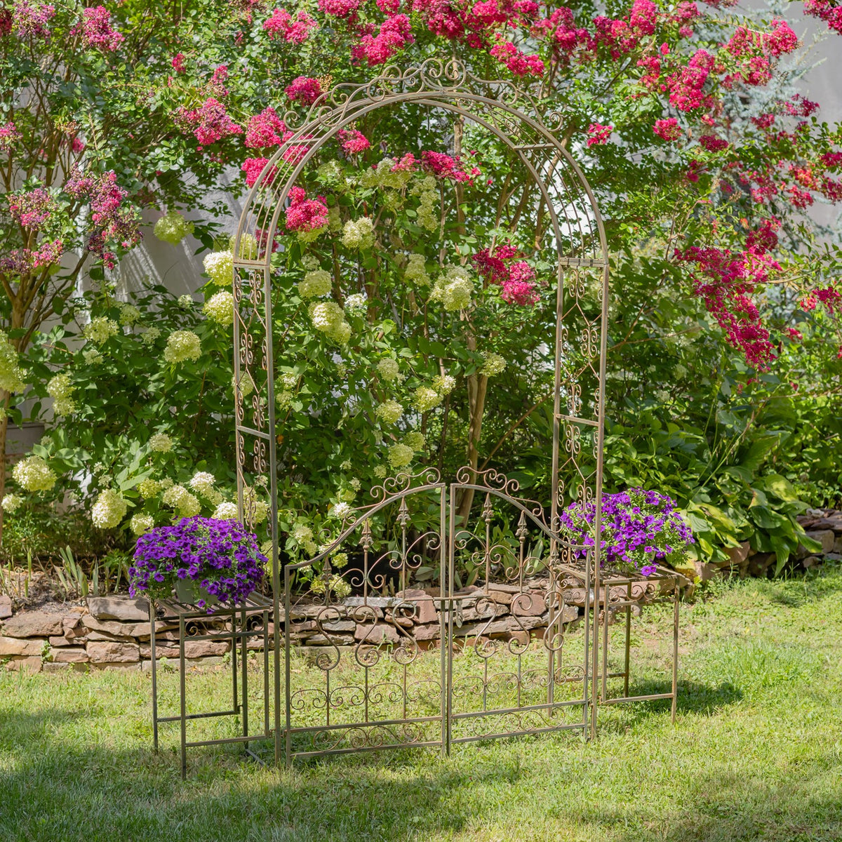 Front view of an ornate iron garden arch and gate among colorful garden plants