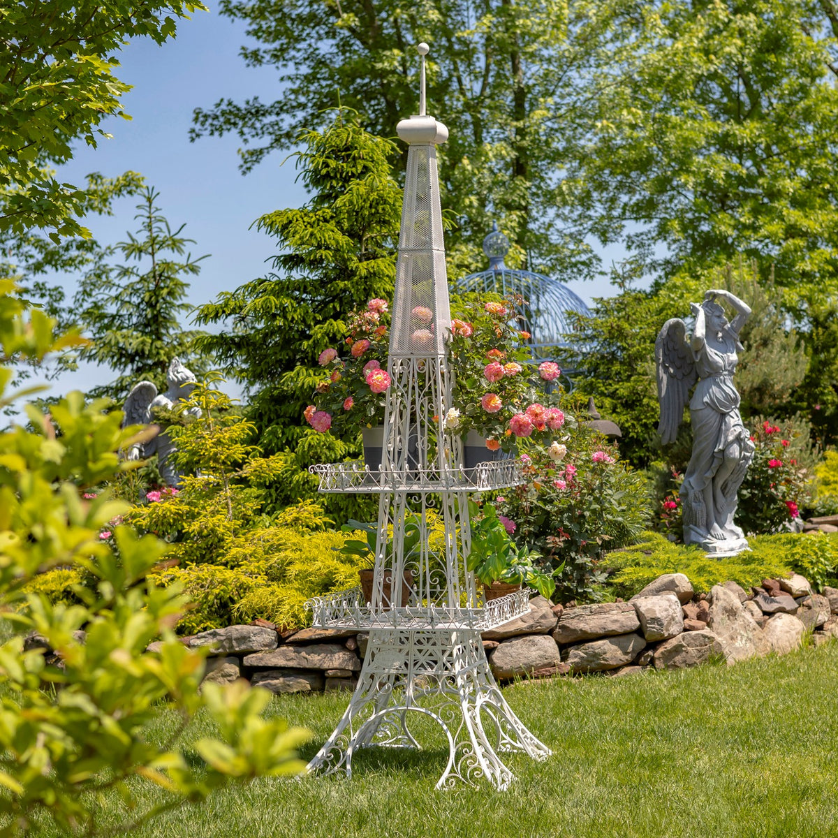 White Eiffel Tower-shaped plant stand with two tiers among flowers and greenery in a sunny garden.