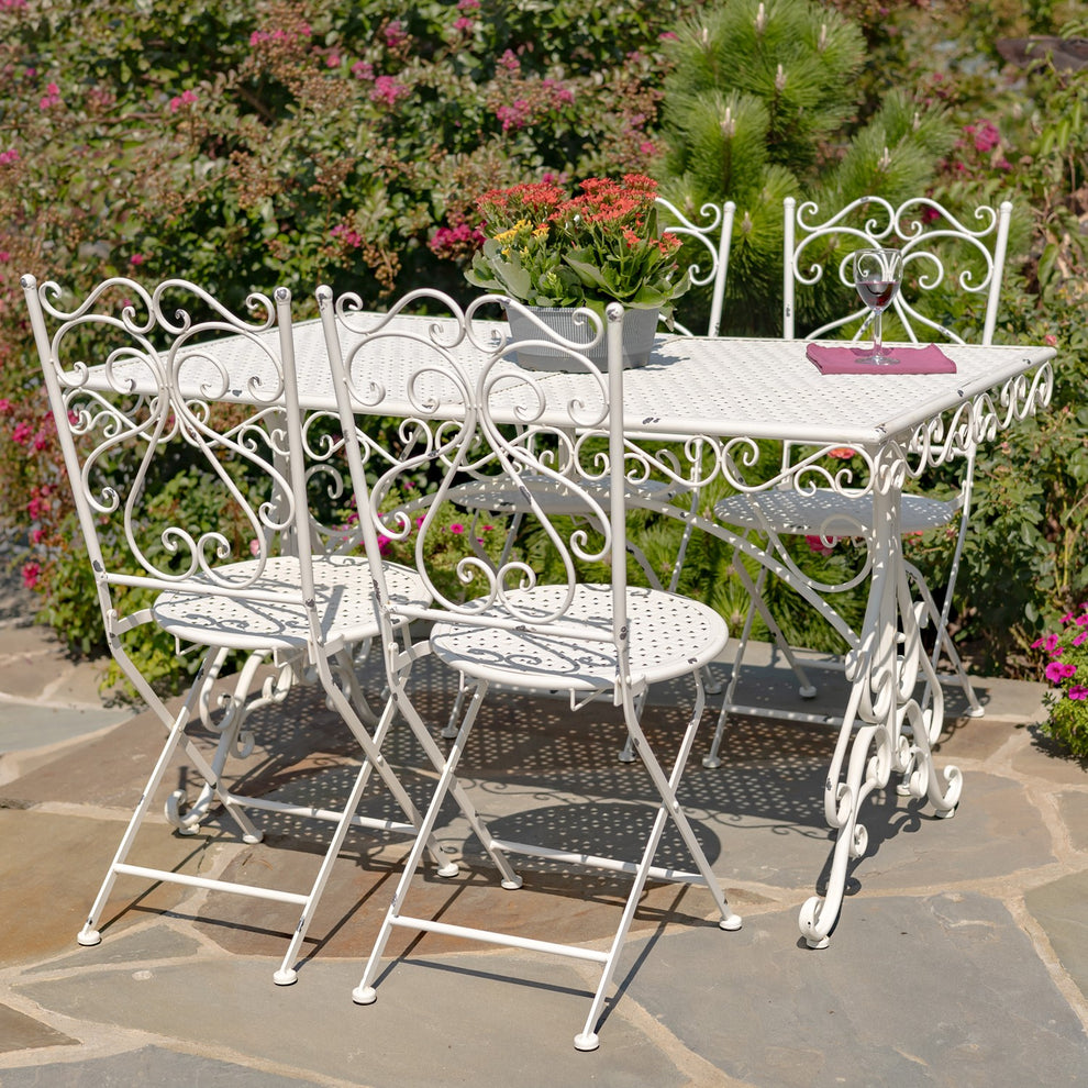 Antique-white metal dining table with four matching scrollwork chairs on a garden patio.
