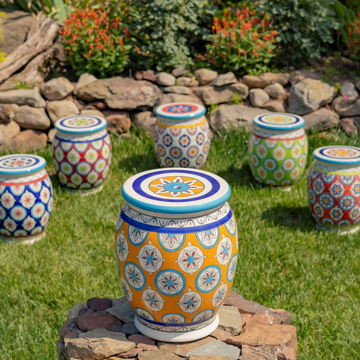 Yellow patterned ceramic stool in front of several colorful stools on a garden lawn.