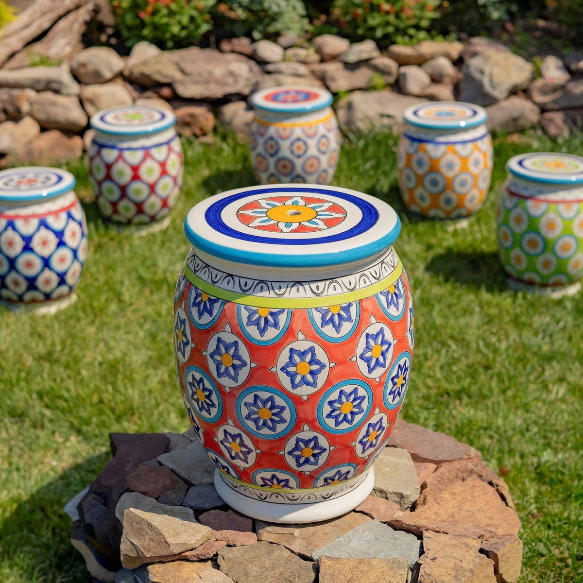 Red patterned ceramic stool on a stone platform, with several colorful stools arranged in the grassy background.