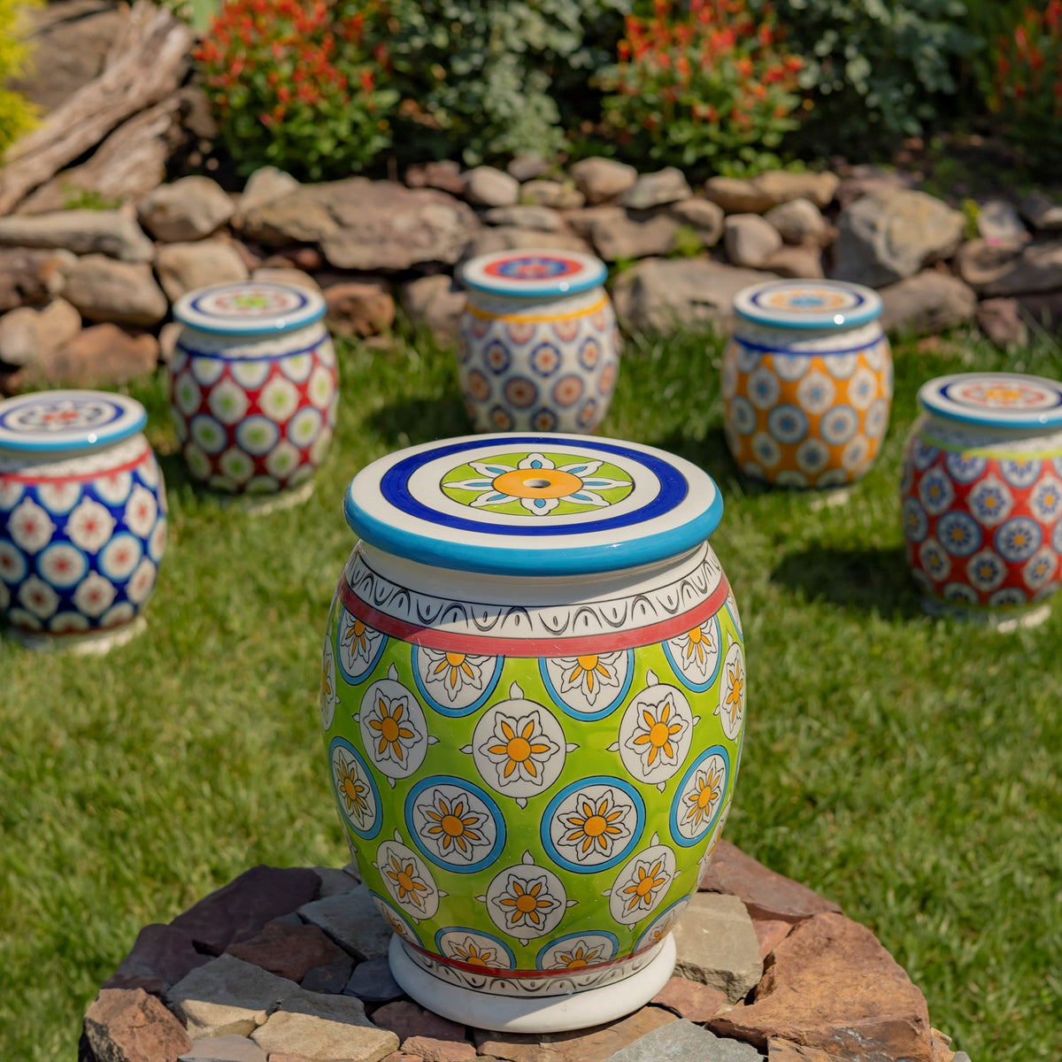 Green floral ceramic stool on a stone platform, with several differently patterned stools arranged in the garden behind it.