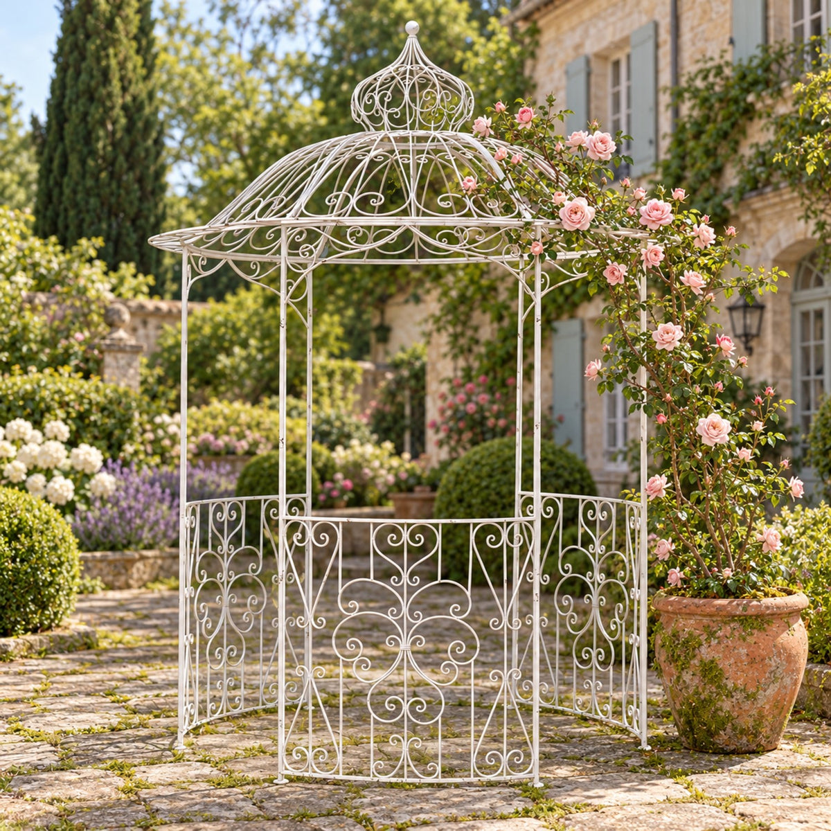 White round iron gazebo with scrollwork among flowers in a garden