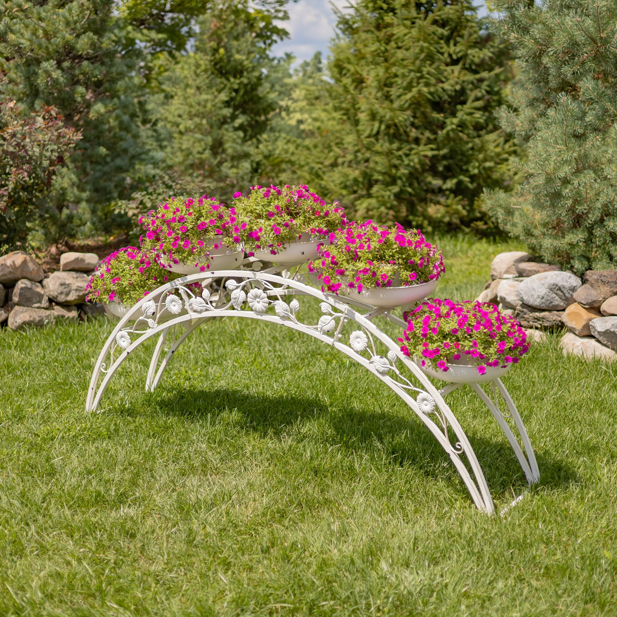 White arched plant stand with flower-filled planters on a lawn in a garden setting.
