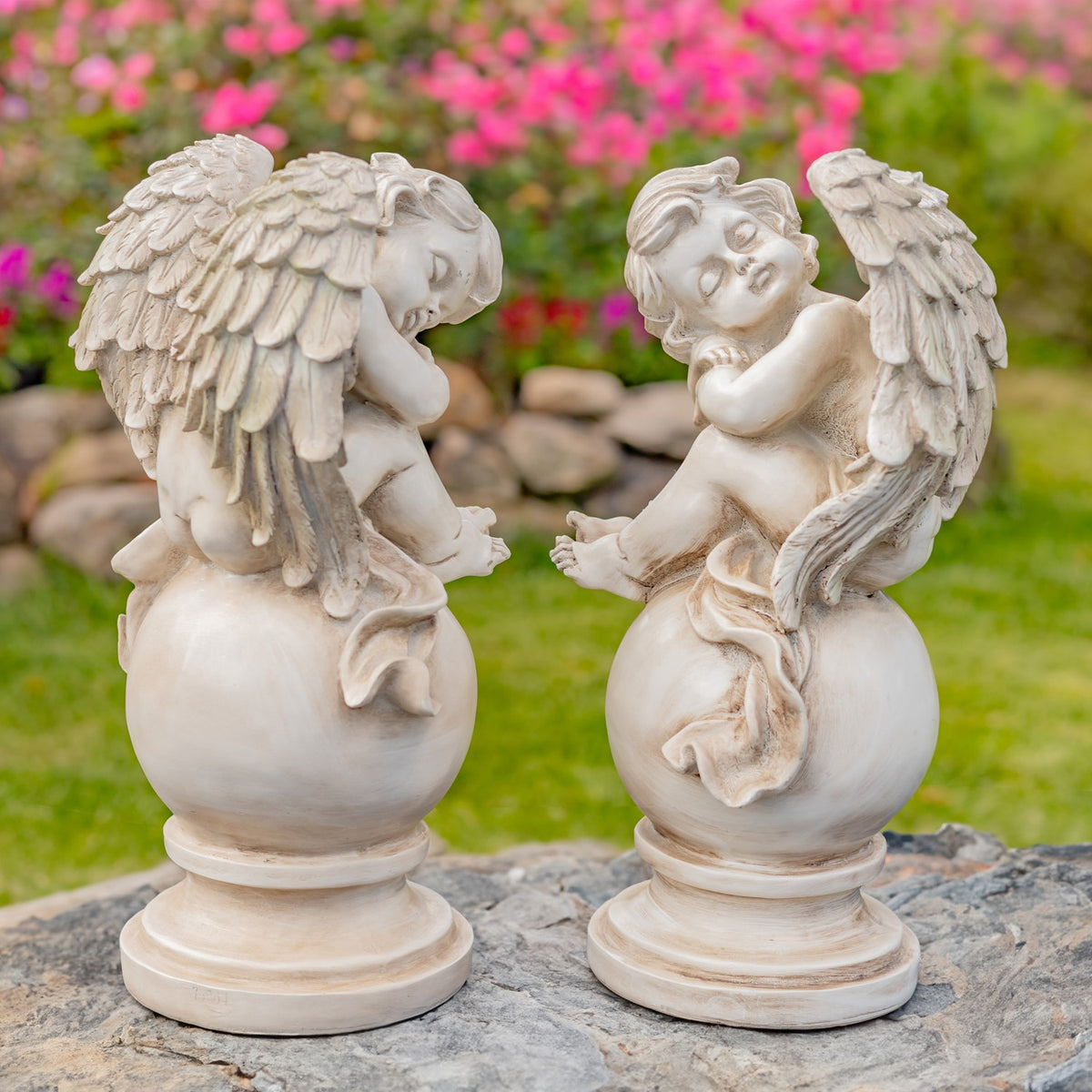Pair of pale distressed cherub statues on globe pedestals outdoors
