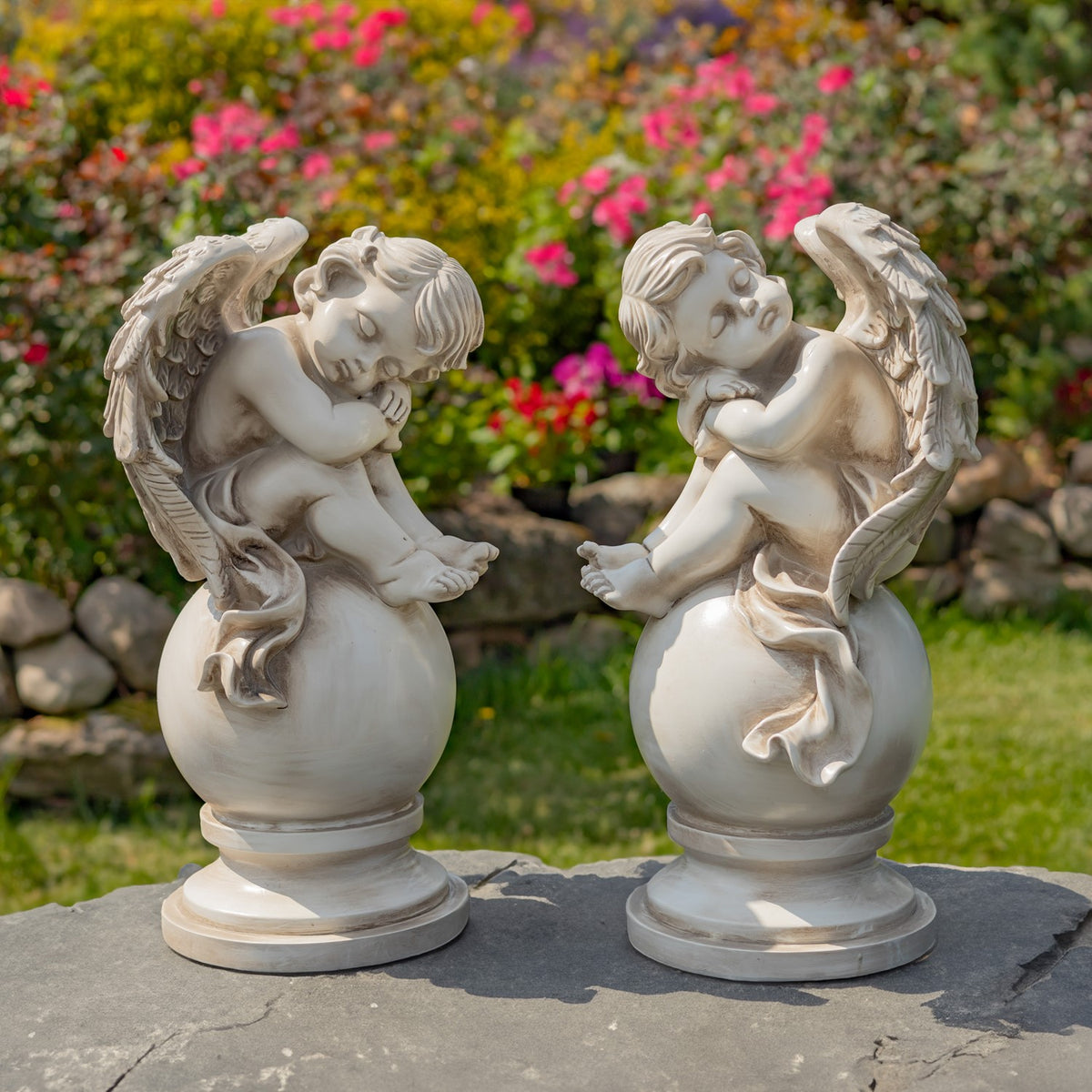 Pair of pale antique-finish cherub statues on globe pedestals in a garden