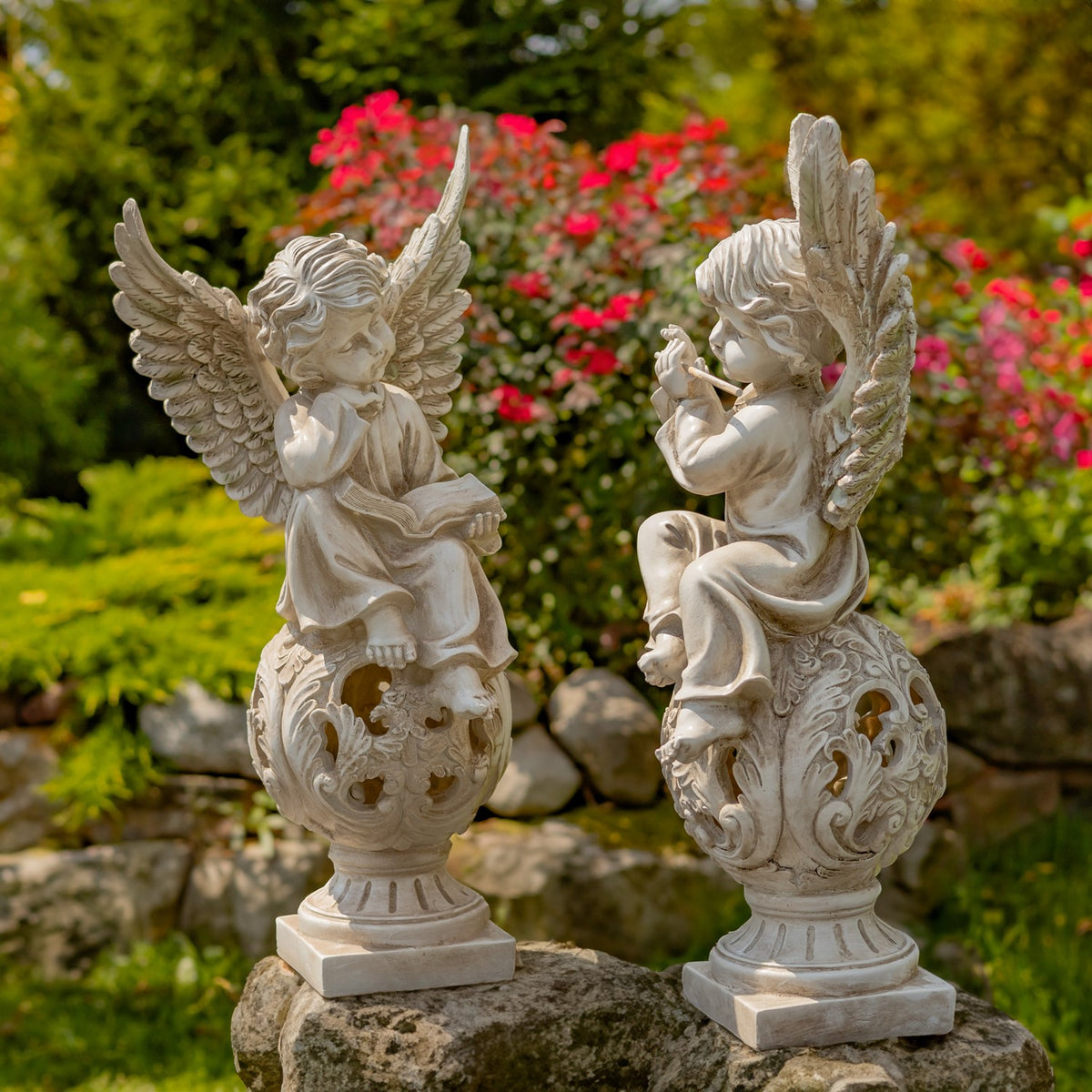 Pair of antique grey cherub statues on openwork pedestals in a garden