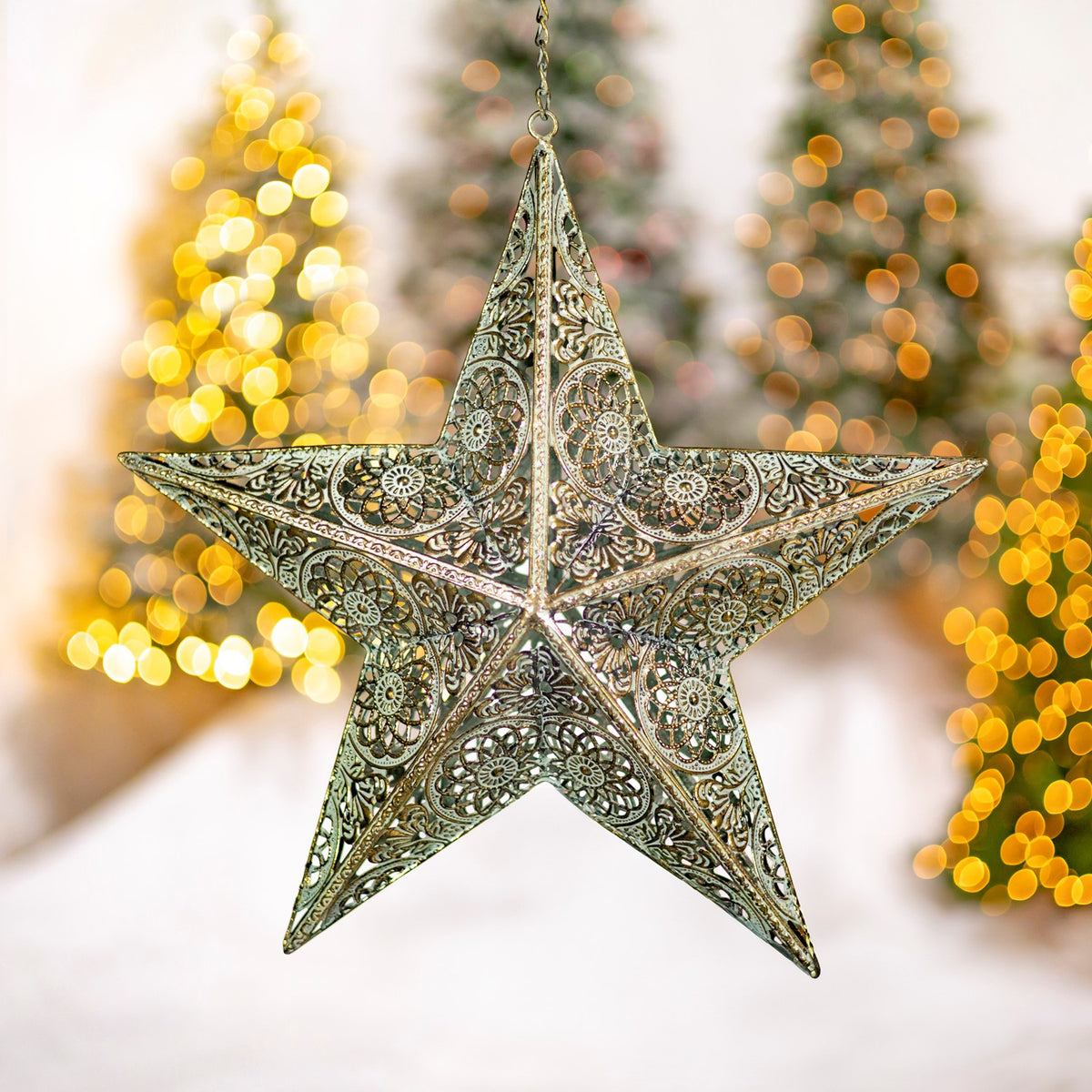 An ornate three-dimensional gold star ornament hangs before softly lit Christmas trees.