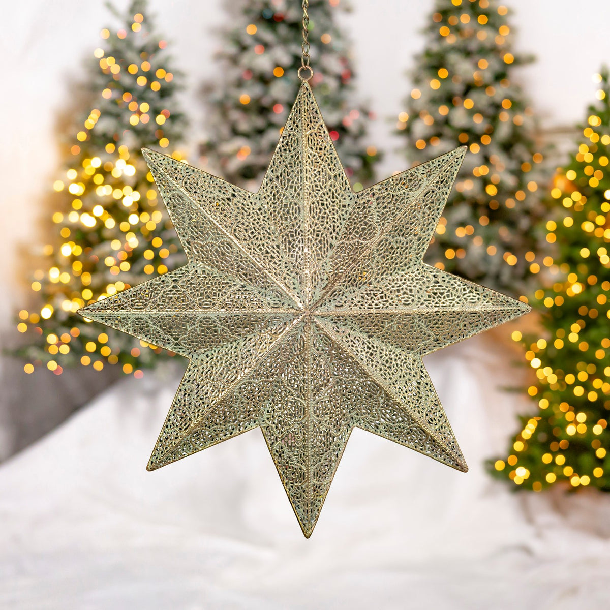 An openwork gold eight-point star ornament hangs in front of softly lit Christmas trees.