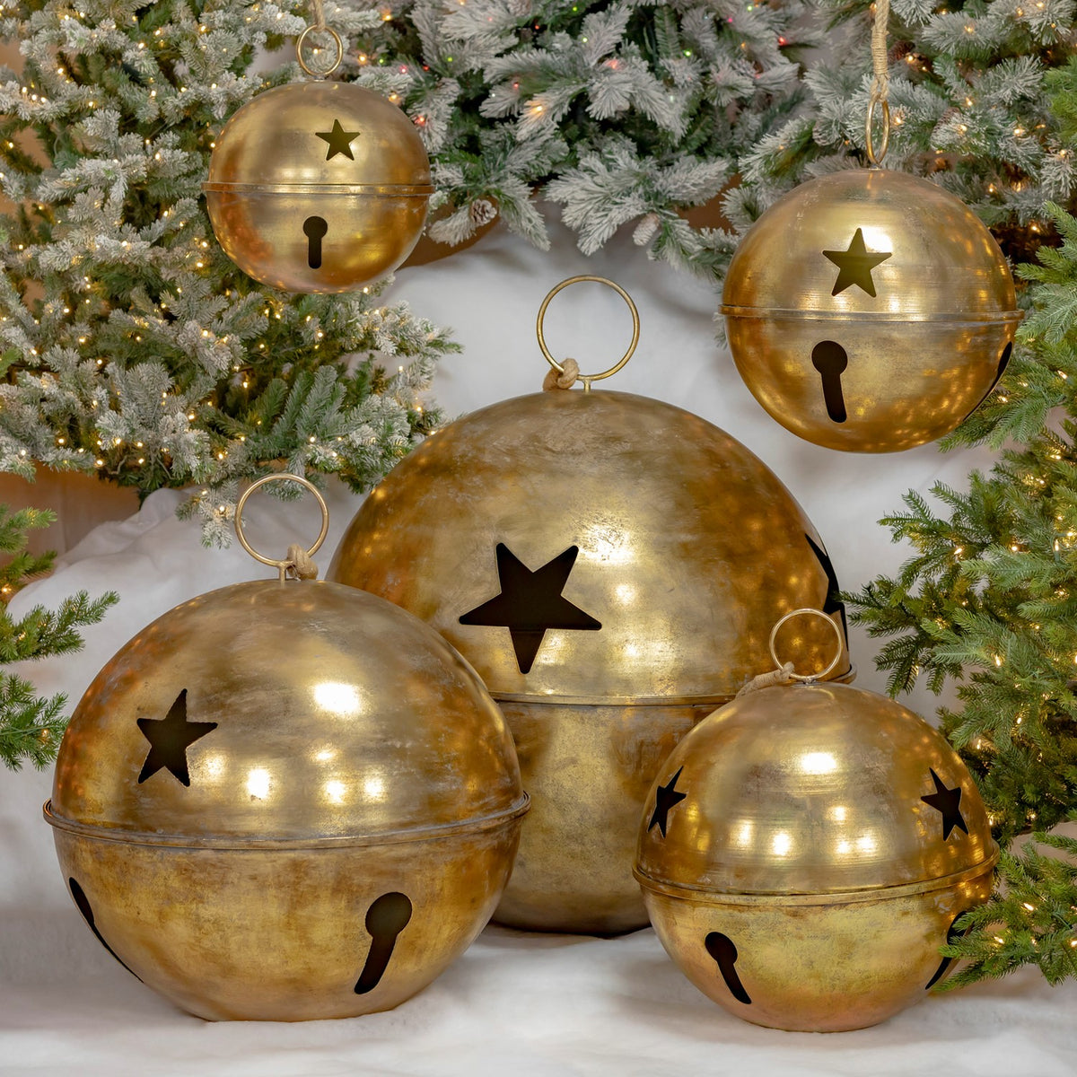 Five antique-gold bells in assorted sizes arranged beneath a lit Christmas tree.