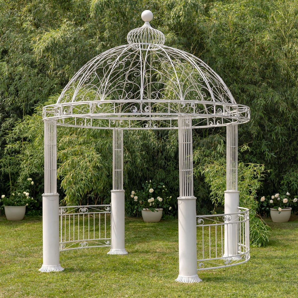 White ornate round iron gazebo with a domed scrollwork roof in a leafy garden.