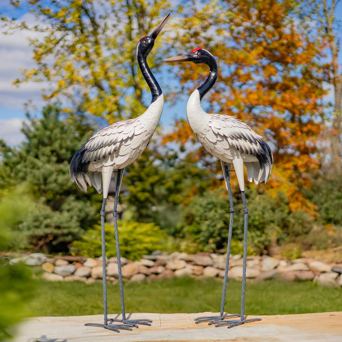 Pair of white crane garden figurines with dark necks standing on a stone patio