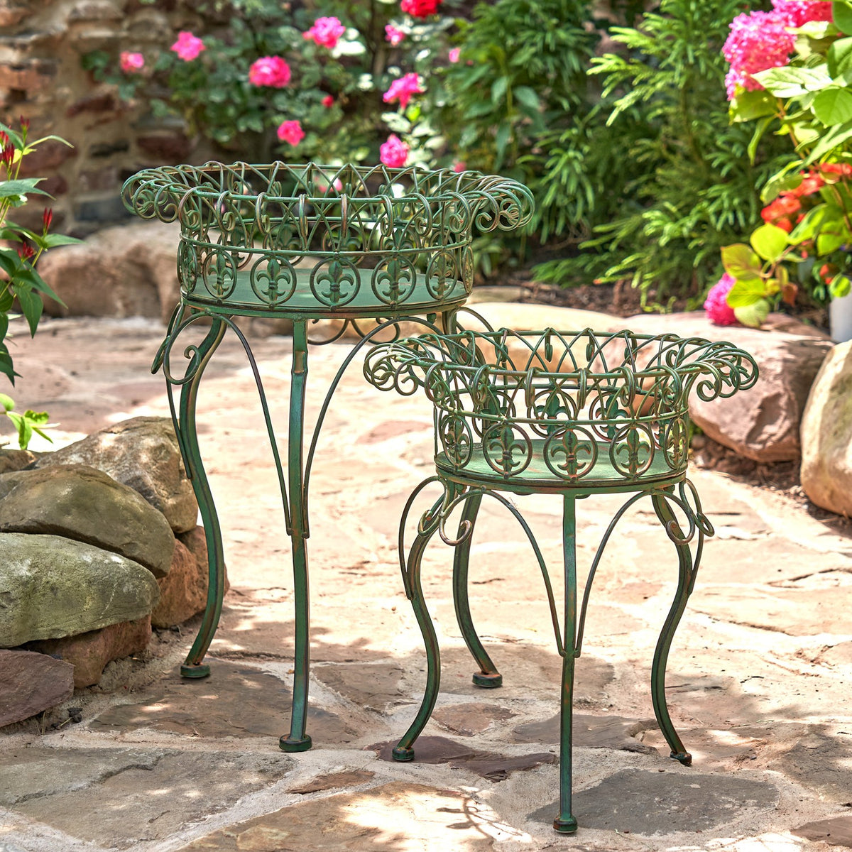 A pair of dark green metal plant stands with circular basket tops displayed on a garden path.