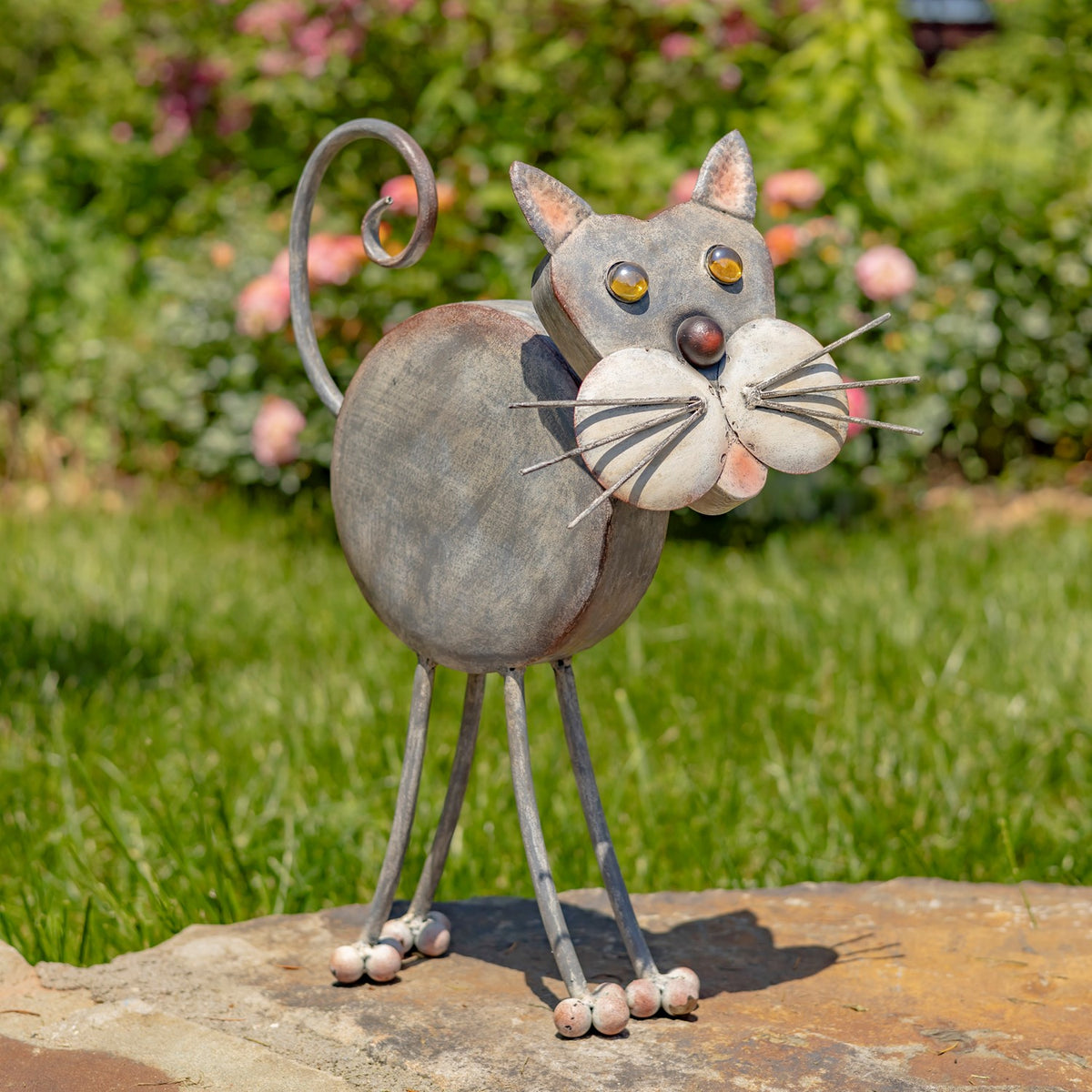 Distressed multicolor iron cat planter standing on a stone slab in a garden