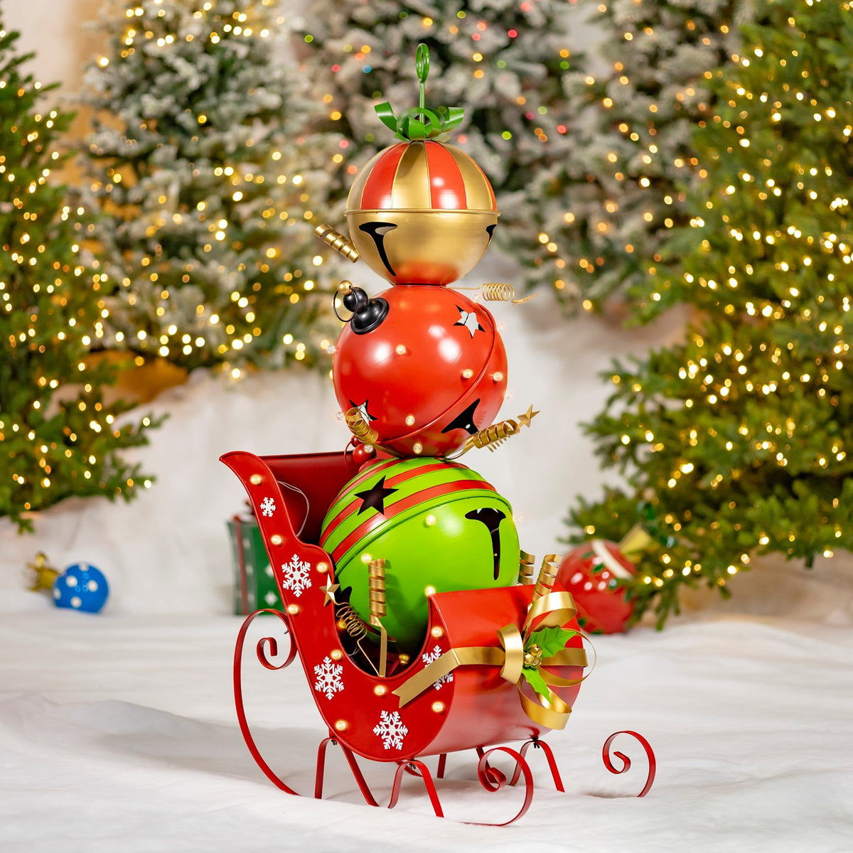 A red sleigh carrying stacked red and green jingle bells stands before a lit Christmas tree.