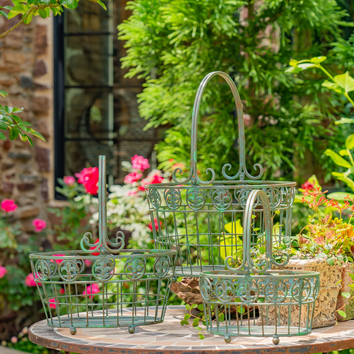 Three green-toned wire baskets with curled decorative rims and handles on an outdoor table.