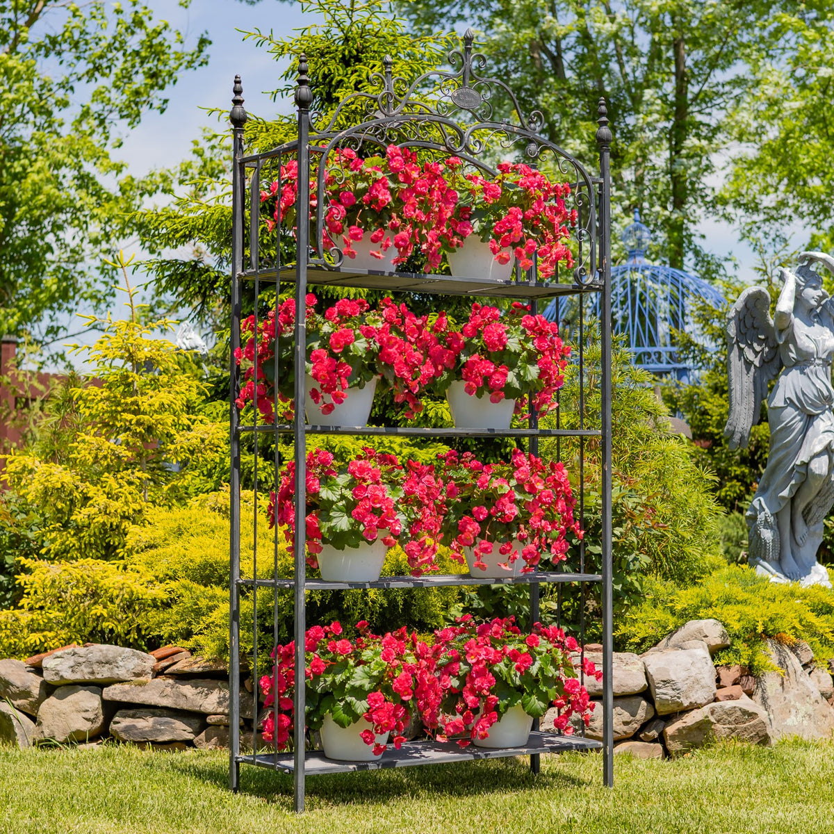 Ornate black iron shelf displaying pots of bright pink flowers in a garden.