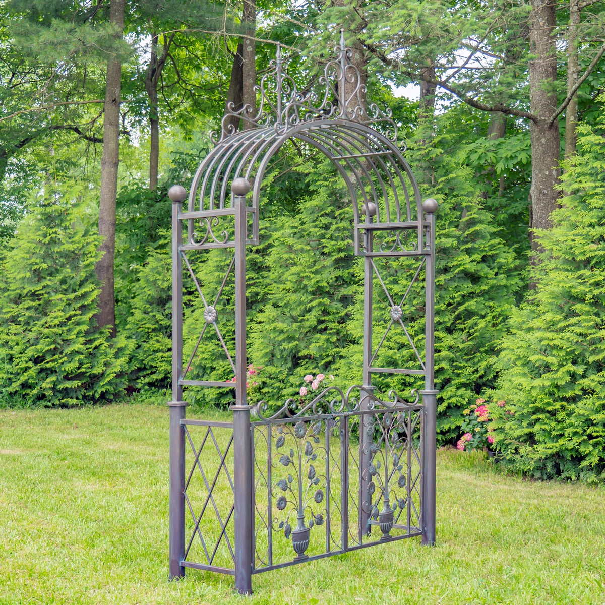 Dark metal garden arch and floral gate shown on a grassy lawn in a leafy garden.