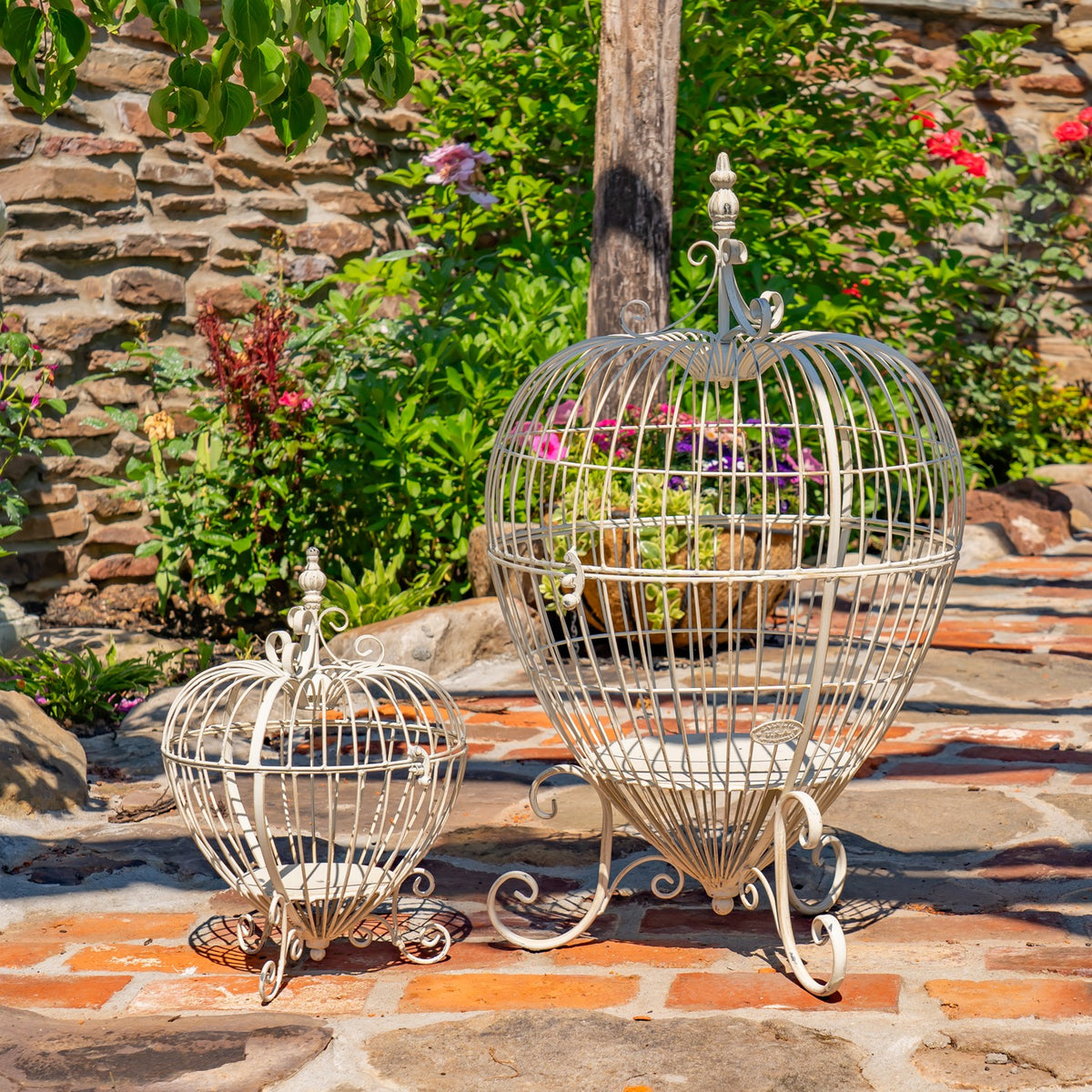 Two ornate wire cage plant stands, one larger than the other, displayed on a garden patio.