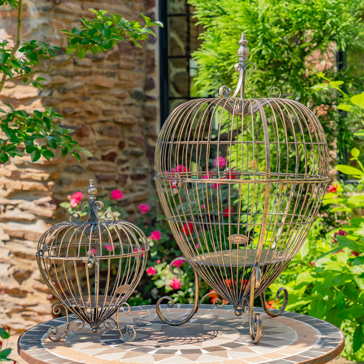A small and a large wire cage stand sit side by side on a round tiled garden table.