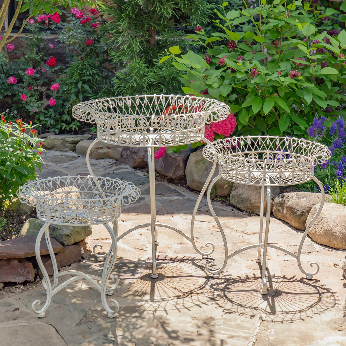 Three pale wire basket stands of different heights arranged on a sunny stone patio.