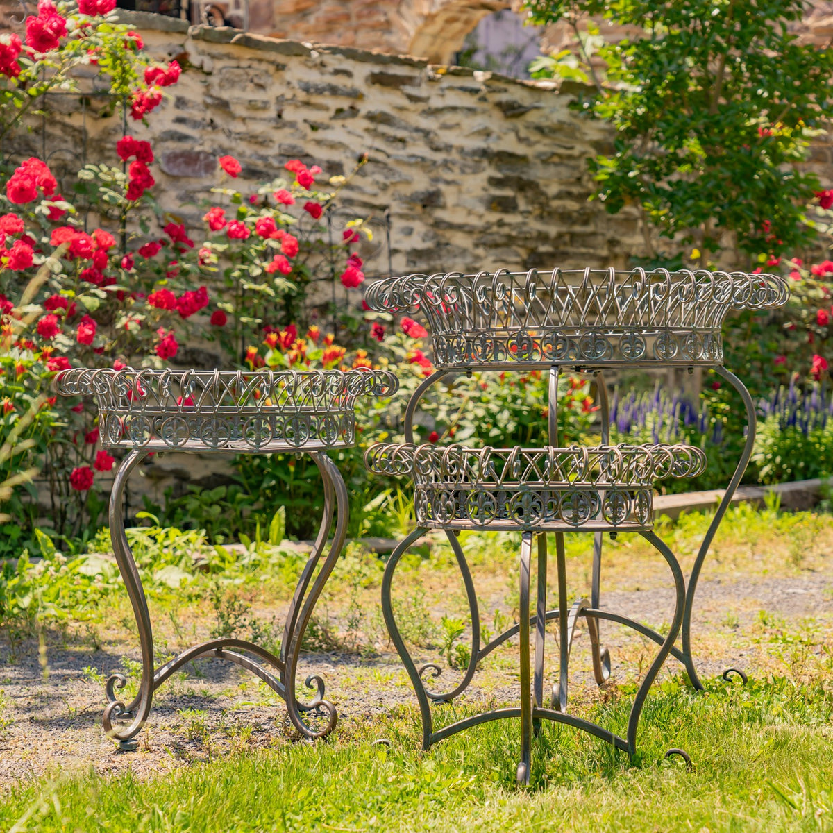 Three ornate round wire basket stands arranged at different heights among flowering garden plants.