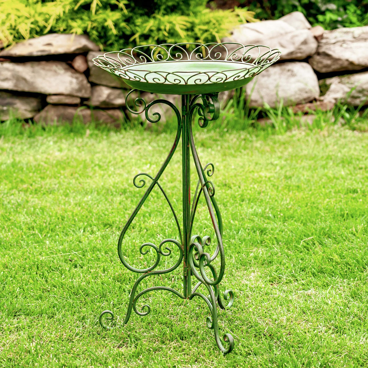 Dark green scrollwork birdbath and three-legged stand displayed on a lawn.
