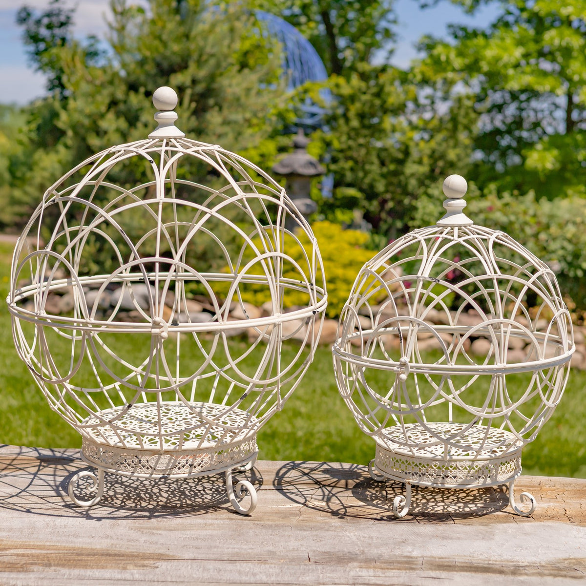 Pair of antique white wire globe plant stands displayed outdoors on a wooden table