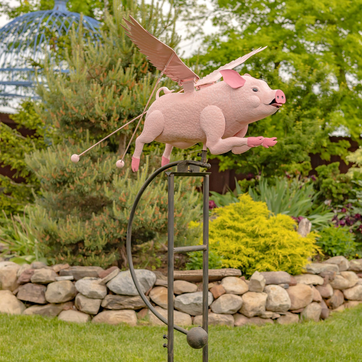 Pink flying pig stake shown from the side in a landscaped garden