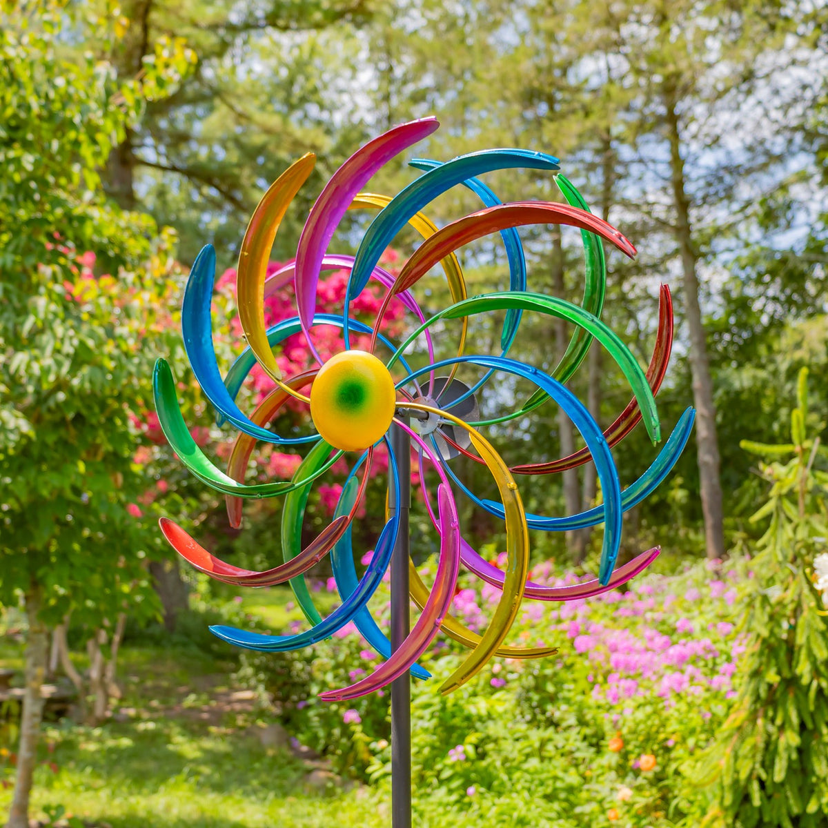 Multicolored metal windmill stake viewed from the front in a flowering garden