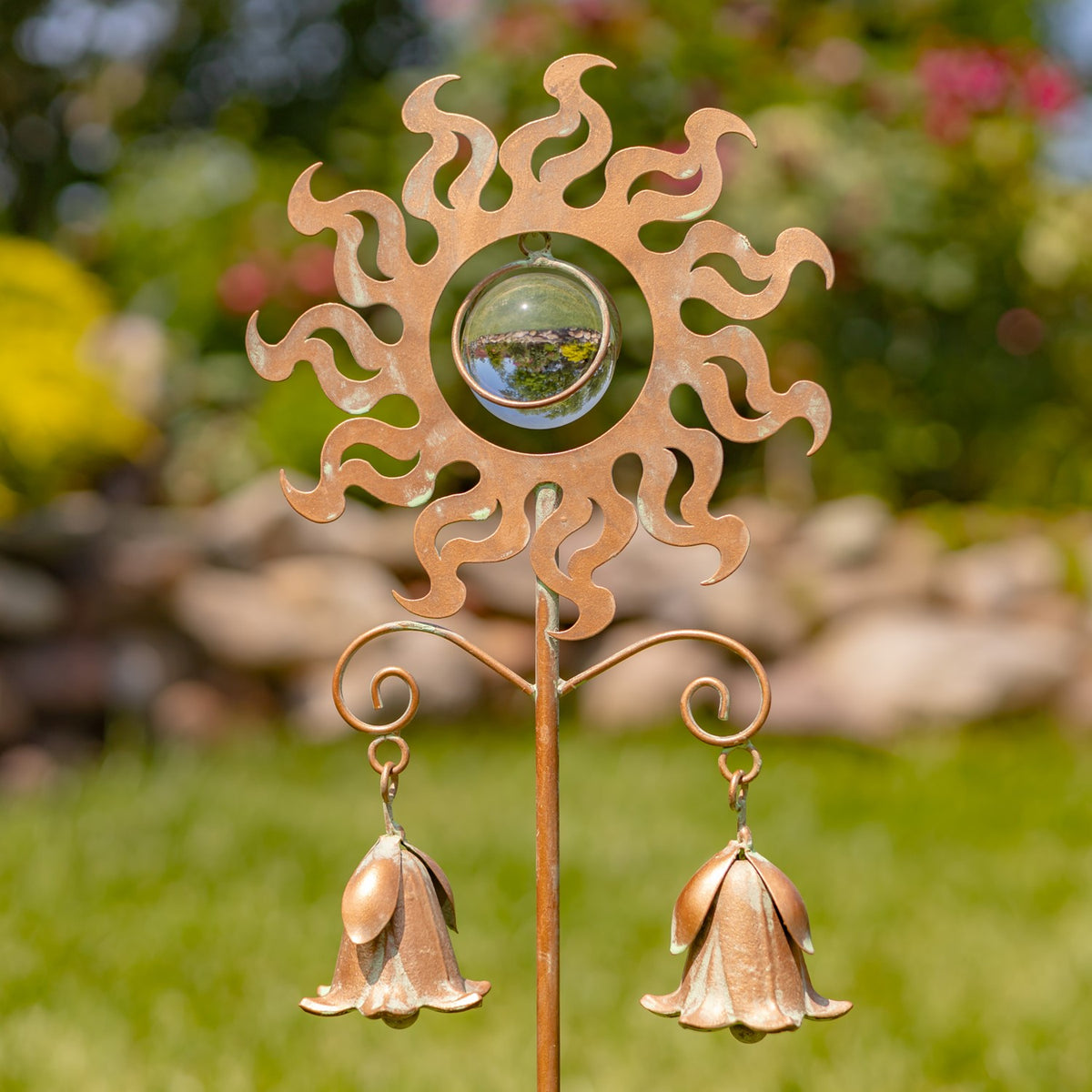 Copper-toned sun garden stake with a reflective center and two hanging lily-shaped bells.