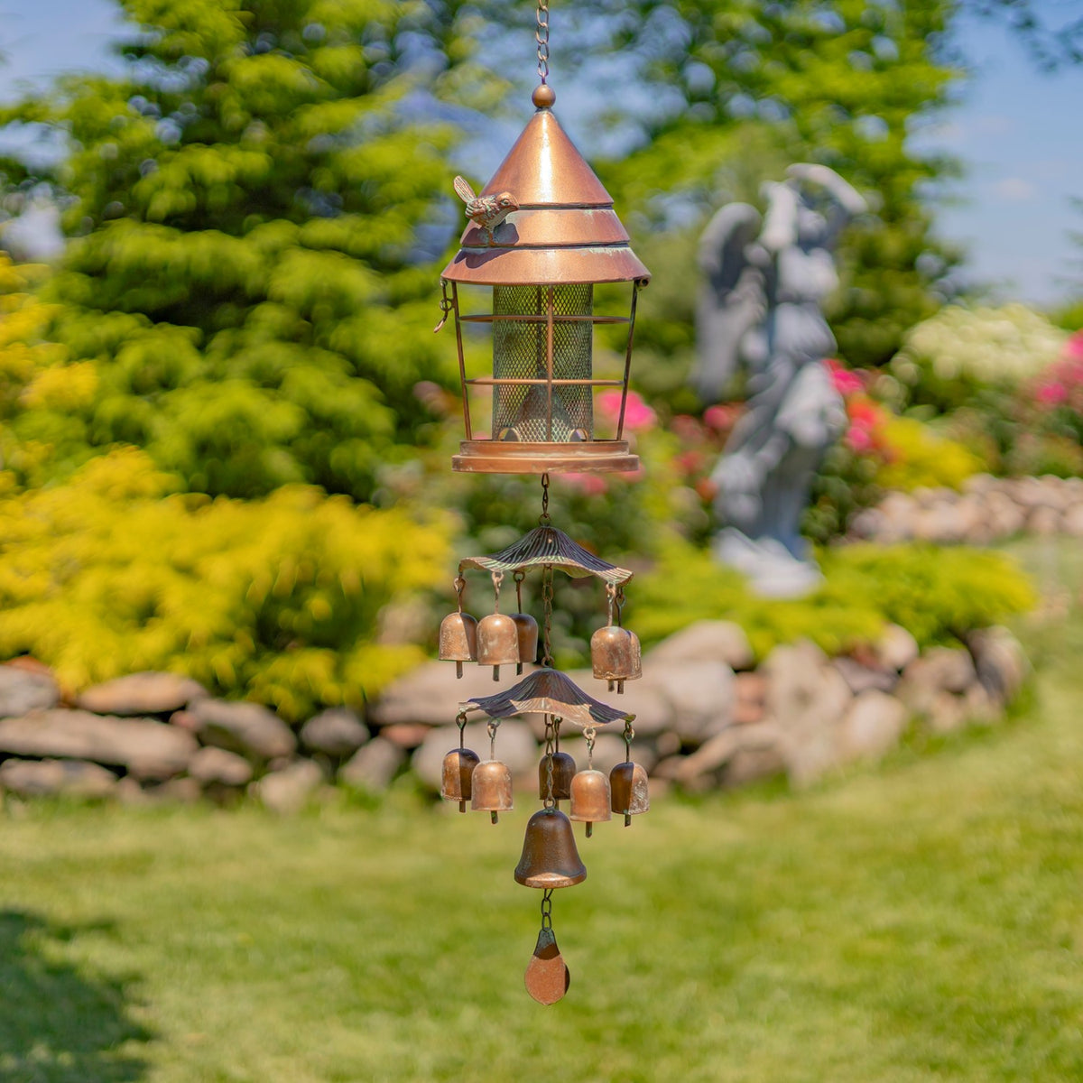 Copper-toned hanging birdfeeder with dangling chimes in a garden