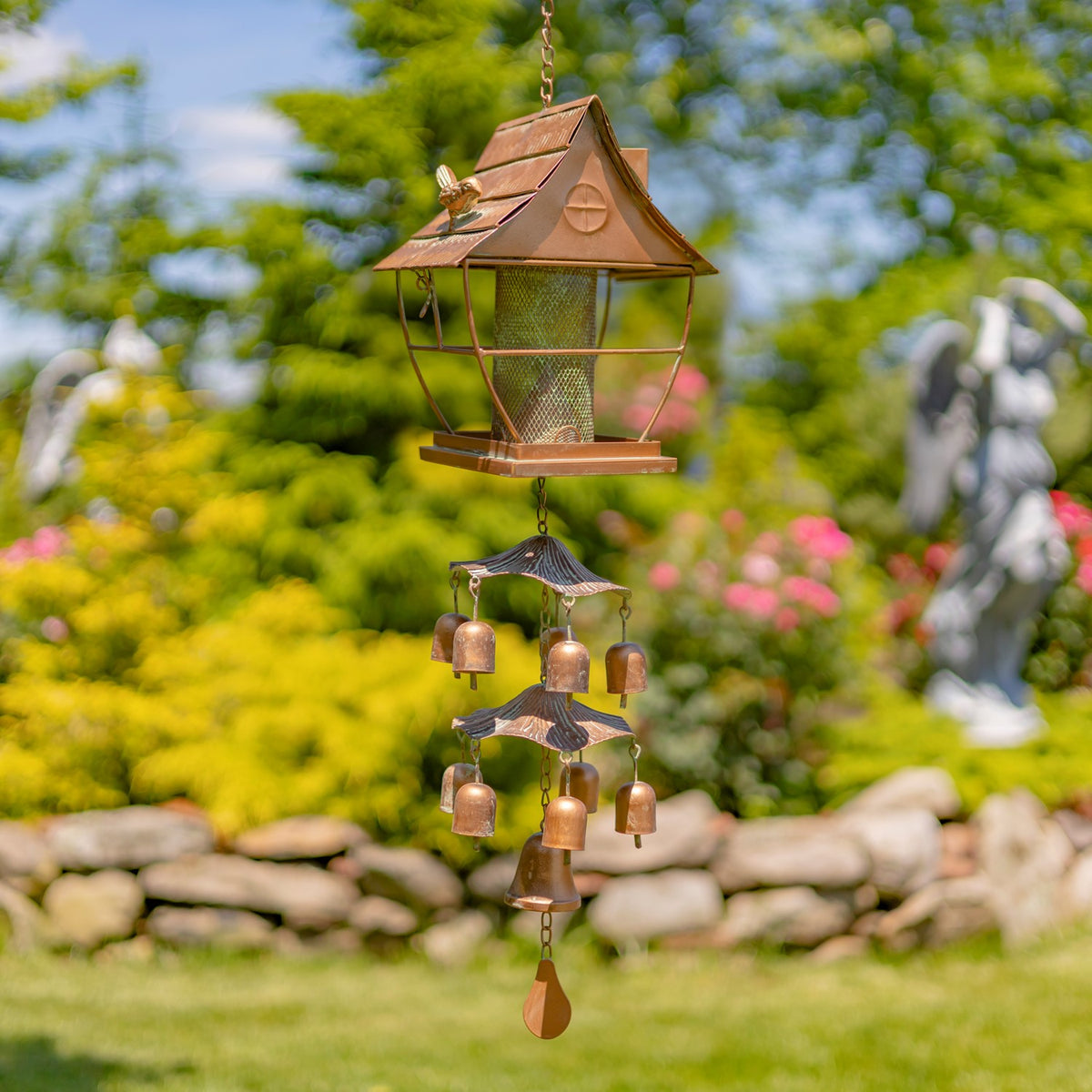 Hanging pagoda-style bird feeder with a tiered bell chime beneath it, shown in a garden.