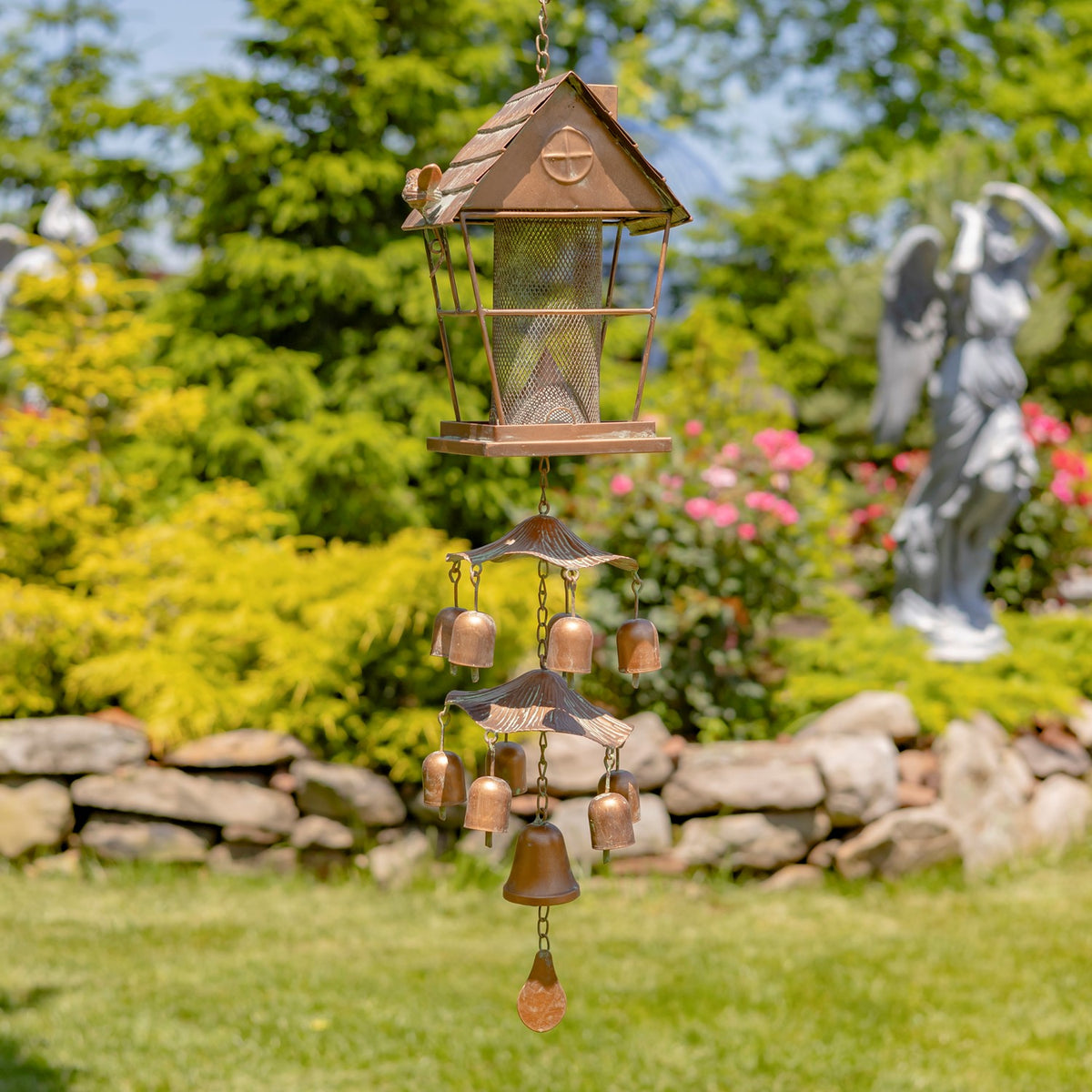 Hanging metal bird feeder with tiered bell chime in a green garden