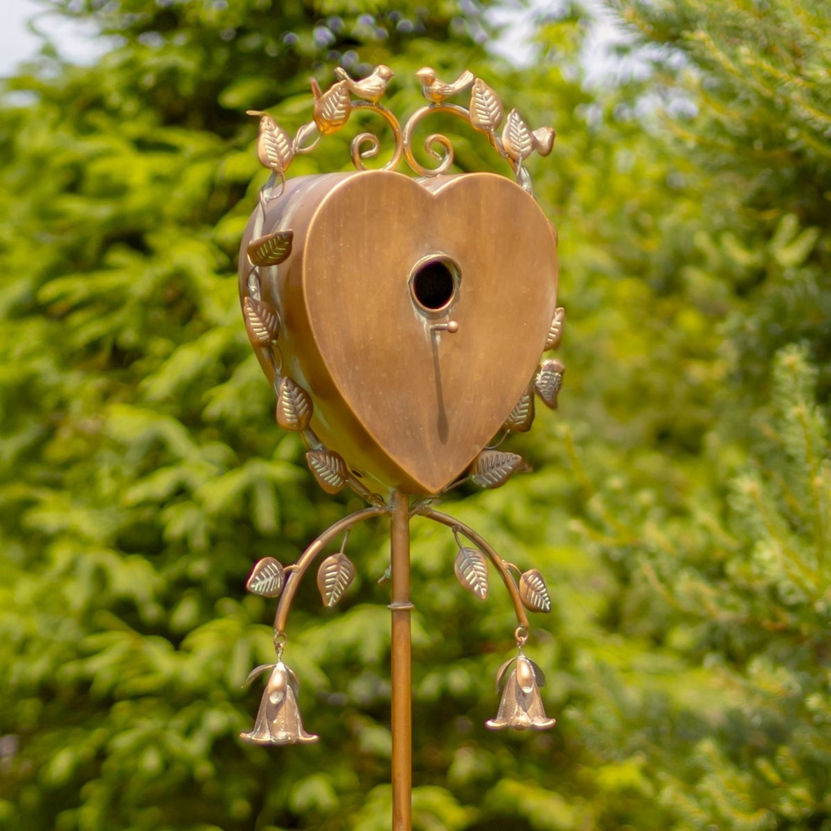 Heart-shaped metal birdhouse with a round entrance, leaf accents, birds, and two dangling bells.