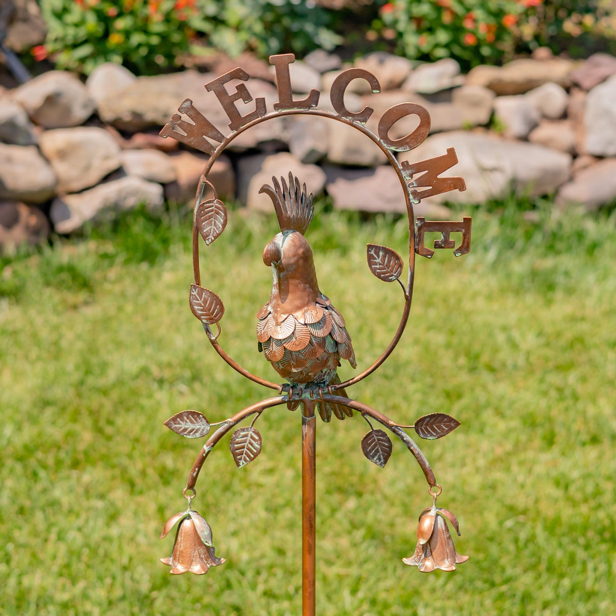 Rust-toned garden stake with a metal cockatoo inside a circular frame, leafy accents and two dangling bells.