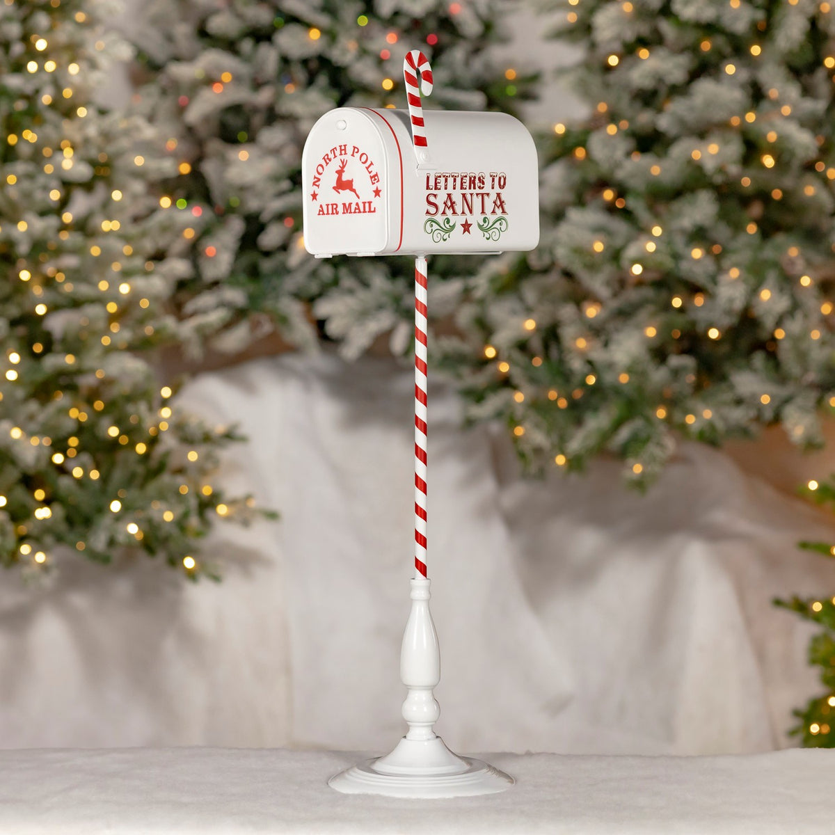 White mailbox on a red-and-white striped stand, displayed in front of lit Christmas trees.
