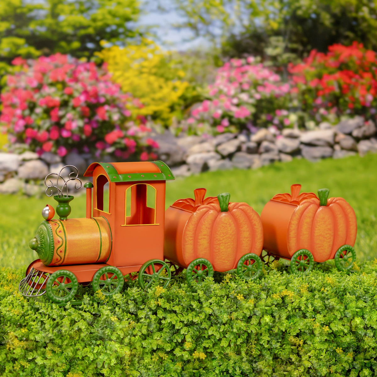 Orange-and-green pumpkin train with two pumpkin carts displayed among garden plants and flowers.