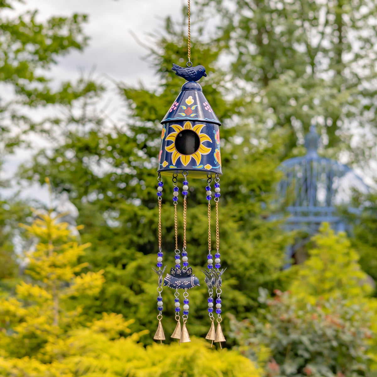 Blue birdhouse wind chime with yellow flower accents and beaded strands hanging in a garden.
