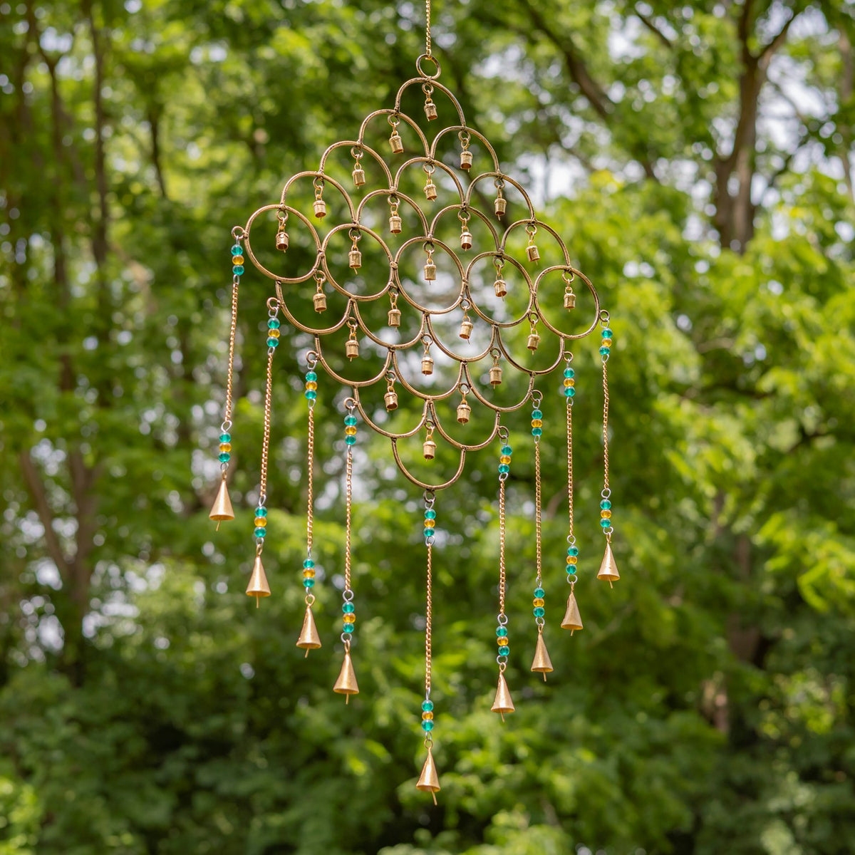 Gold circular wind chime with turquoise and yellow beads hanging against leafy trees.