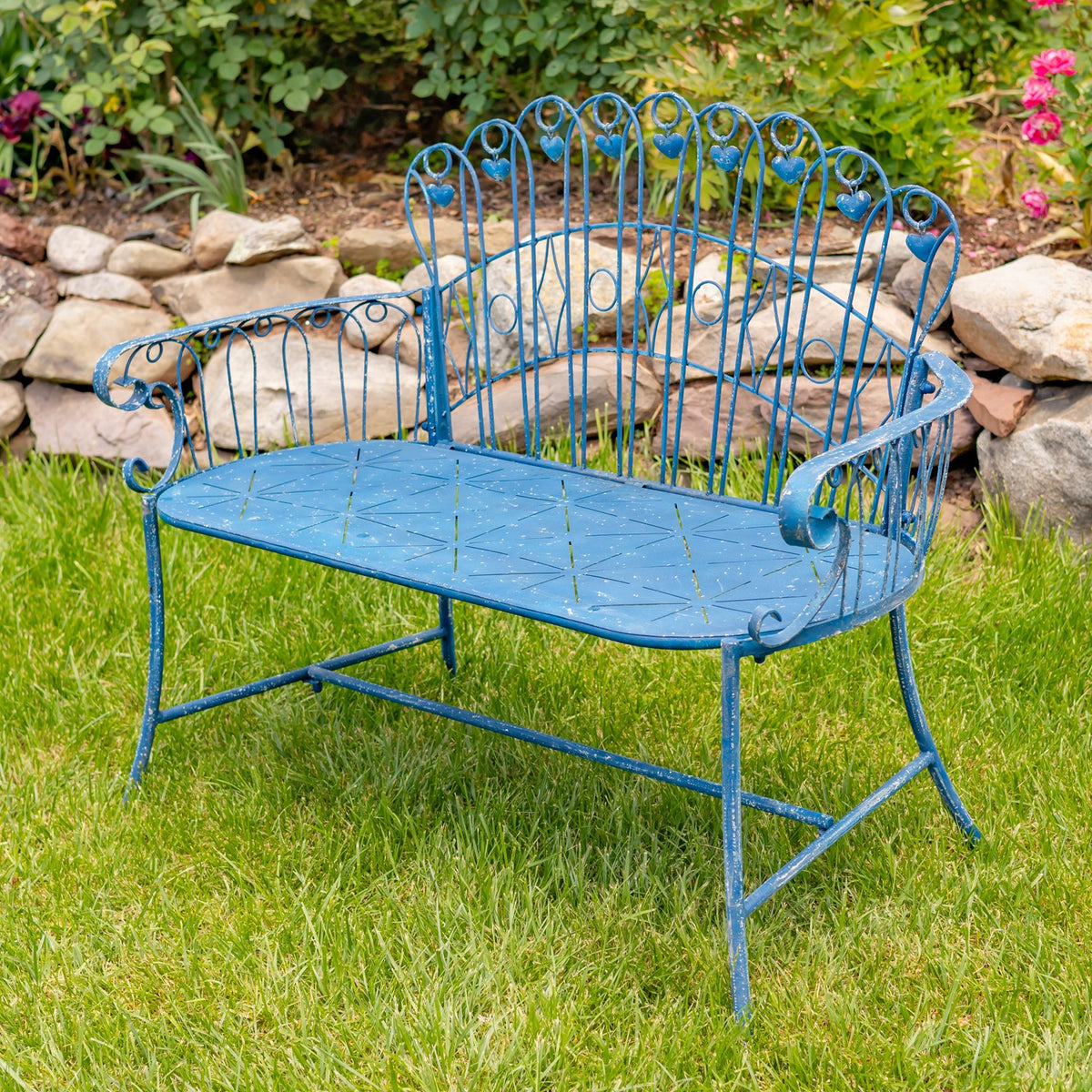 Distressed blue iron garden bench angled view on grass beside a stone garden border