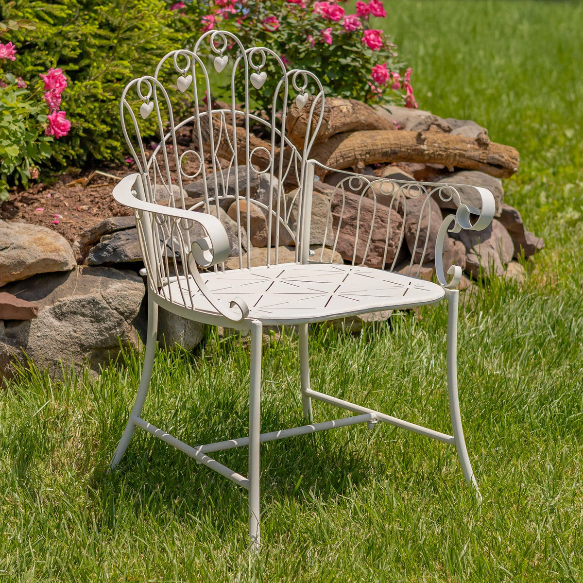 Ivory metal garden armchair with curled arms and heart-shaped back details on a lawn.