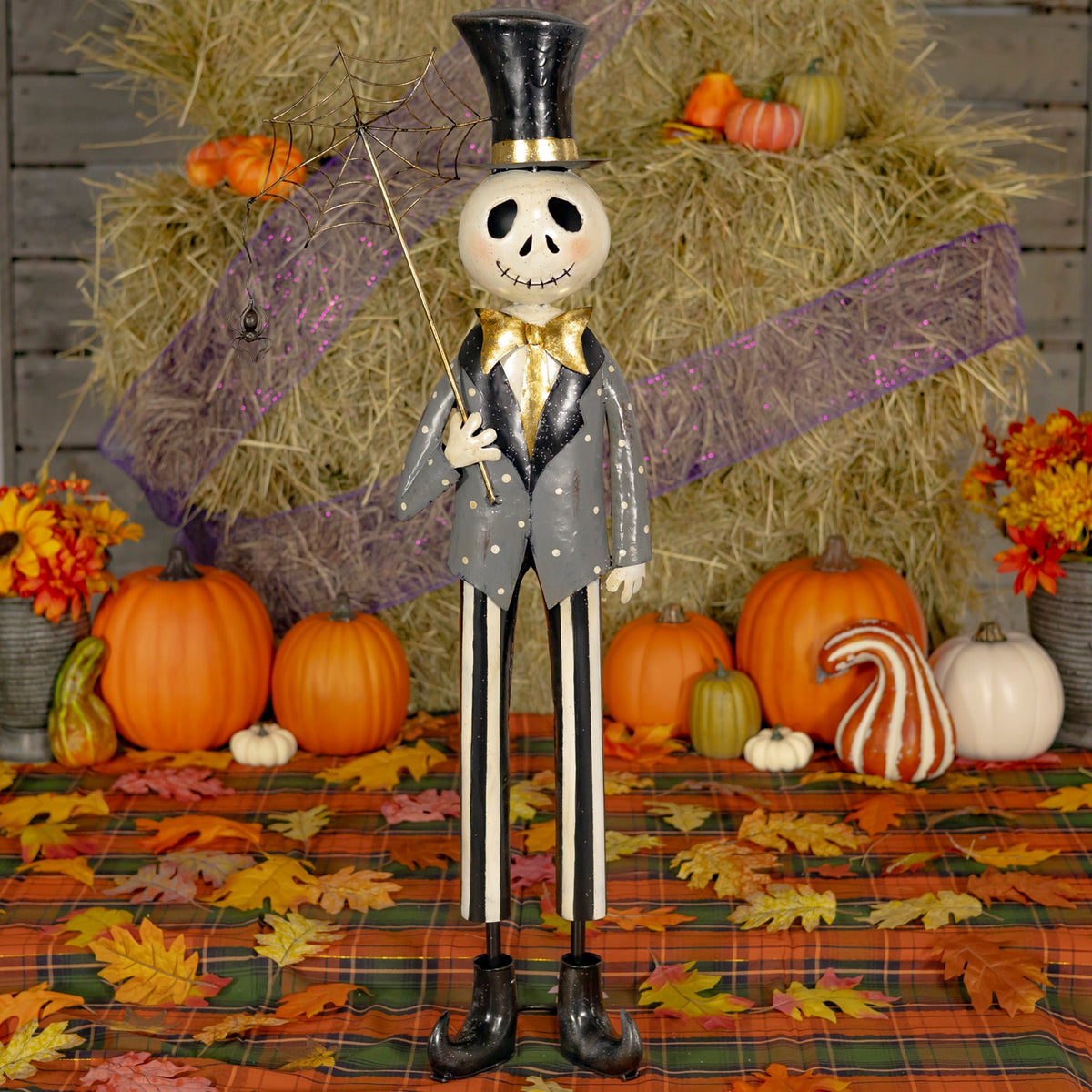 Full view of a skeleton boy with a spiderweb umbrella in a pumpkin-filled Halloween display