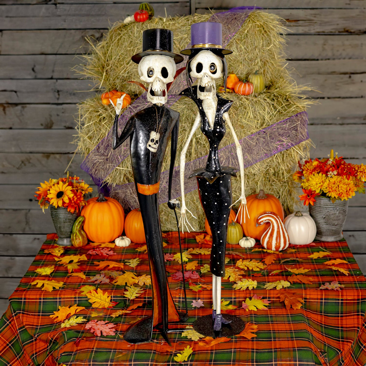 Pair of black-and-white skeleton figurines standing among pumpkins and autumn decorations