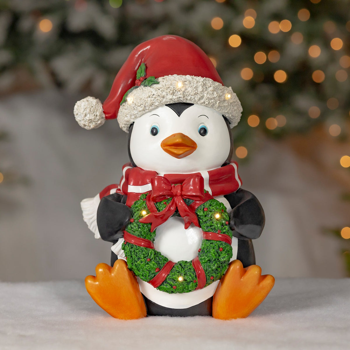 Seated penguin decoration wearing a Santa hat and scarf, holding an illuminated green wreath.