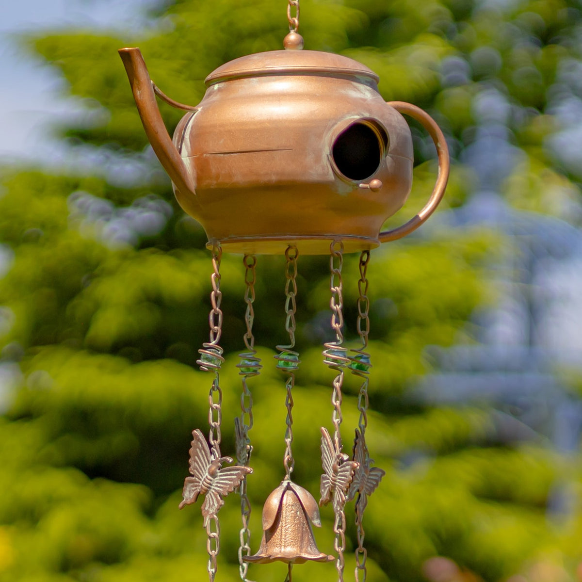Copper-colored teapot wind chime with a round bird opening, hanging chains, bird ornaments, and a bell.
