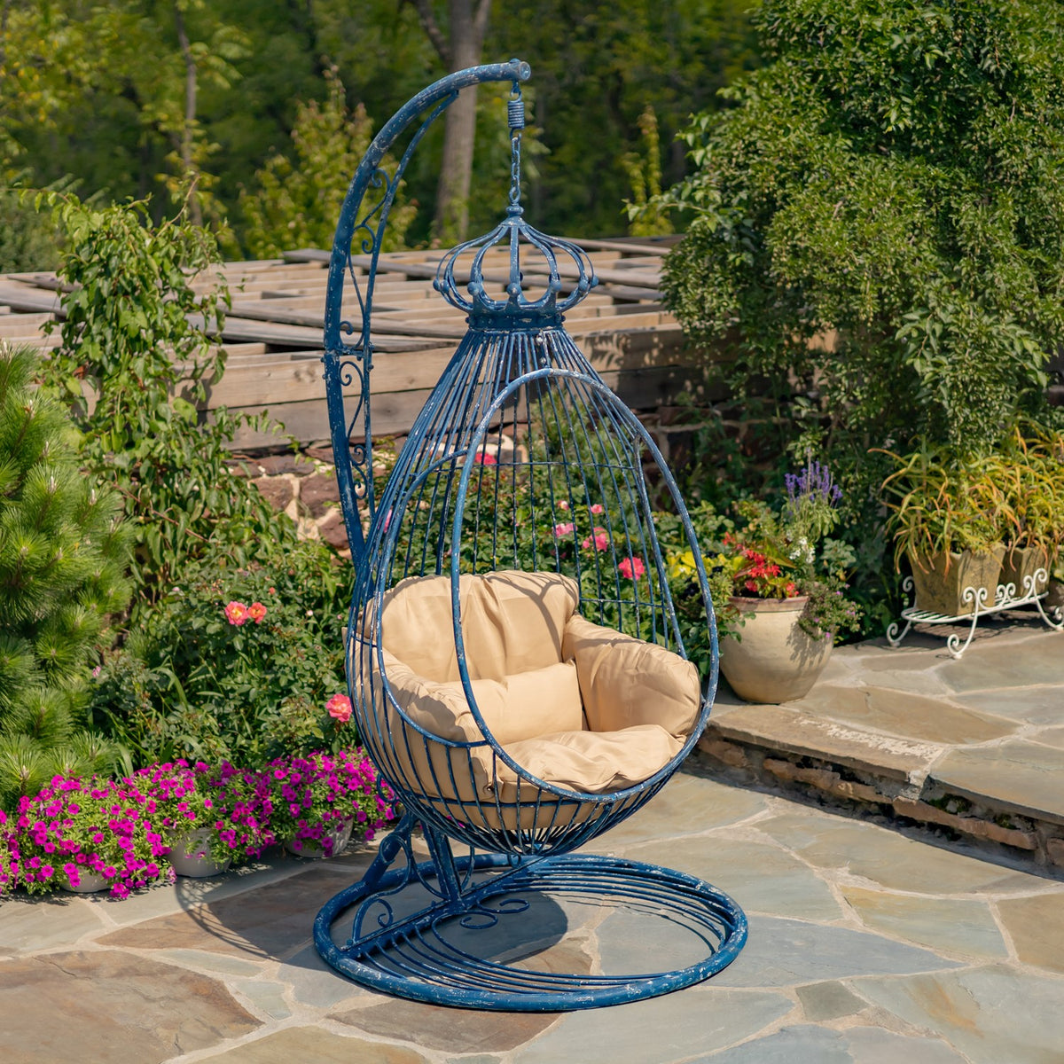 Blue metal egg chair with a tan cushion and circular stand on a garden patio.